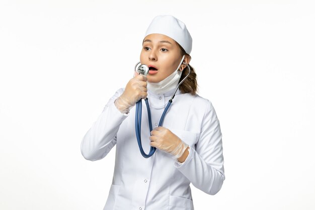 Front view young female doctor wearing protective sterile mask due to coronavirus on white surface