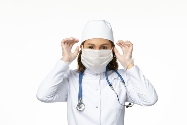 Front view young female doctor wearing protective sterile mask due to coronavirus on white surface