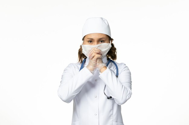 Вид спереди молодой женщины-врача в защитной стерильной маске из-за коронавируса на белой поверхности