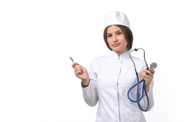 A front view young female doctor in white medical suit and white cap with blue stethoscope posing 