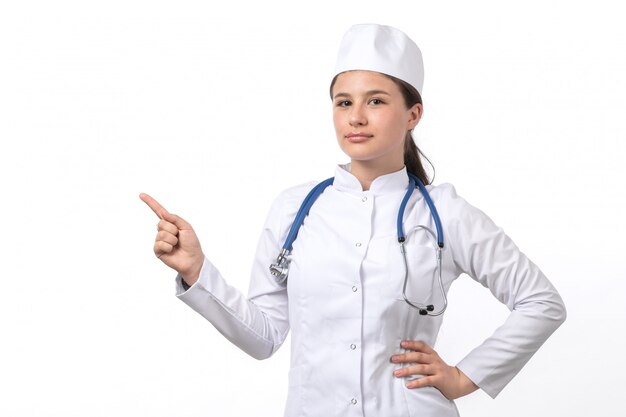 A front view young female doctor in white medical suit and white cap with blue stethoscope 