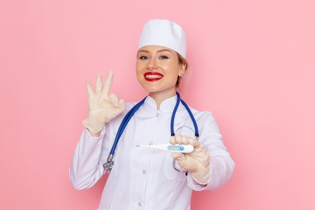 ピンクの宇宙医学病院で笑顔で青い聴診器保持デバイスと白い医療スーツの正面若い女医