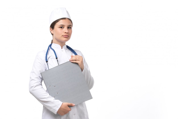 A front view young female doctor in white medical suit with blue stethoscope holding documents 