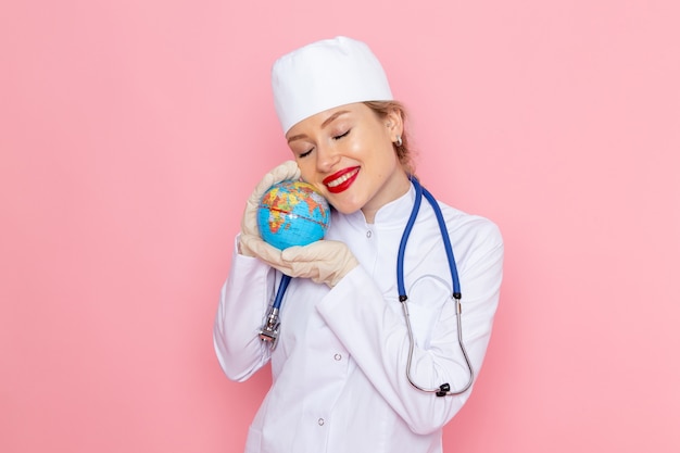 Front view young female doctor in white medical suit with blue stethoscope holding globe with smile on the pink space medicine medical hospital health worker