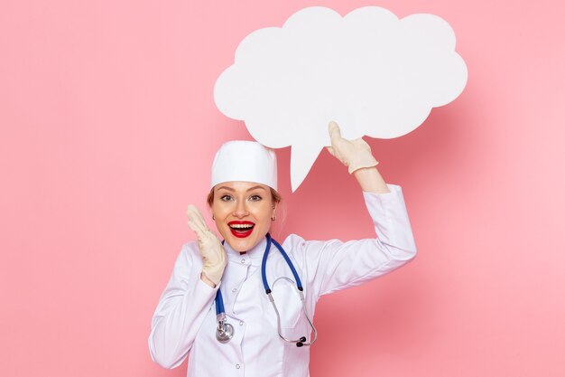 Front view young female doctor in white medical suit with blue stethoscope holding huge white sign with smile on the pink space medicine medical hospital health work