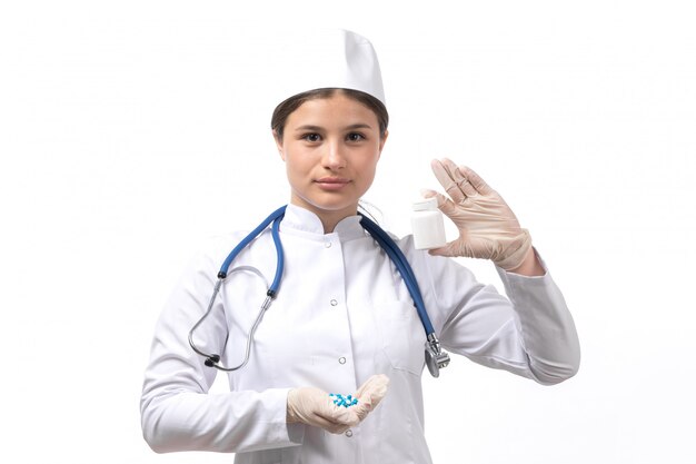 Вид спереди молодая женщина-врач в белом медицинском костюме с голубой стетоскоп, держа таблетки