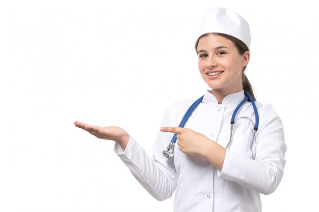 A front view young female doctor in white medical suit with blue stethoscope posing with smile 