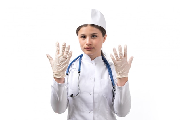 Вид спереди молодая женщина-врач в белом медицинском костюме с синим стетоскопом, показывая перчатки
