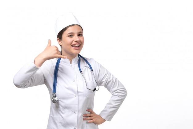 Вид спереди молодая женщина-врач в белом медицинском костюме с голубой стетоскоп, улыбаясь и позирует