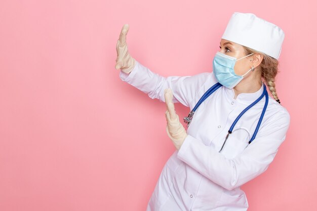 핑크 공간 의학 의료 노동자 간호사에 포즈 멸균 마스크를 쓰고 파란색 청진기와 흰색 의료 정장에 전면보기 젊은 여성 의사