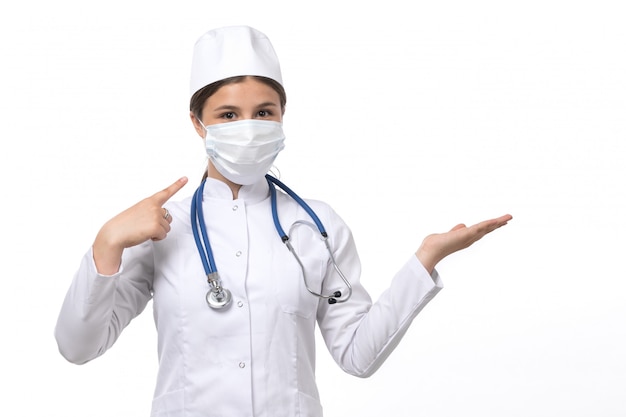 Вид спереди молодая женщина-врач в белом медицинском костюме с голубой стетоскоп в белой маске