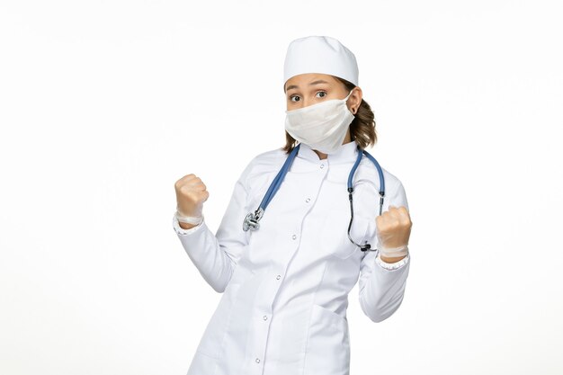 正面図白い医療スーツを着て、明るい白い表面にコロナウイルスによる滅菌マスクを着用した若い女性医師