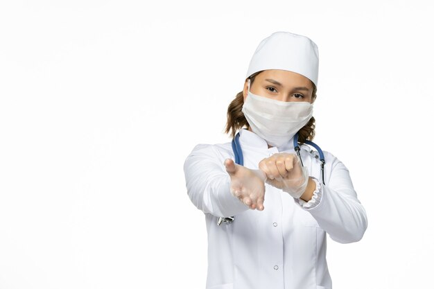 正面図白い医療スーツを着て、明るい白い表面にコロナウイルスによる滅菌マスクを着用した若い女性医師