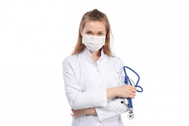 A front view young female doctor in white medical suit with stethoscope wearing white protective mask on the white