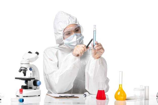 Front view young female doctor in white protective suit with mask due to covid holding blue solution on a white background splash pandemic covid- virus