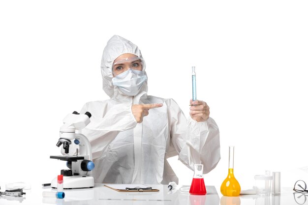白い背景のスプラッシュウイルスパンデミックcovidに青いソリューションを保持しているcovidによるマスクと白い防護服の若い女性医師の正面図