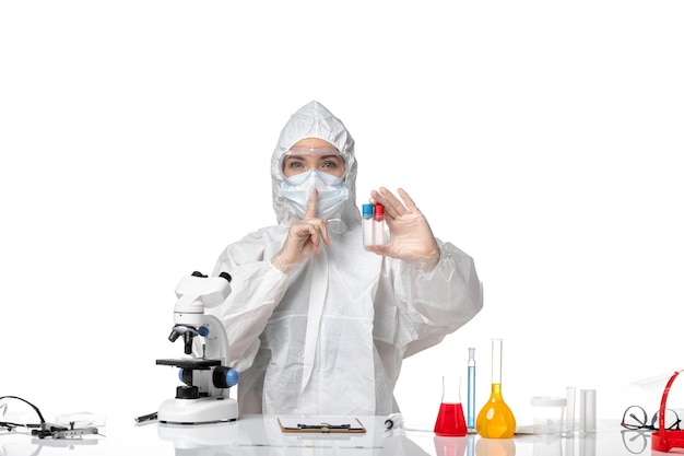 Front view young female doctor in white protective suit with mask due to covid holding empty flasks on a white background pandemic splash virus covid-