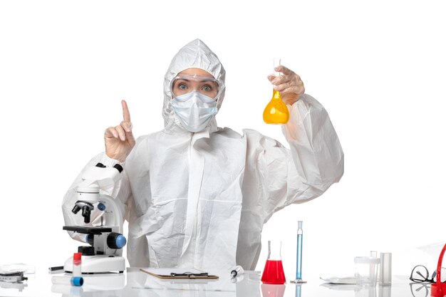 Front view young female doctor in white protective suit with mask due to covid holding yellow solution on a white background splash pandemic covid- virus