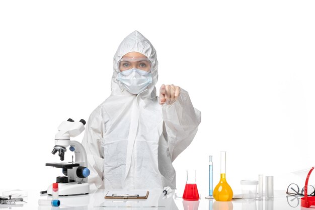 Front view young female doctor in white protective suit with mask due to covid pointing on white background virus pandemic splash covid-