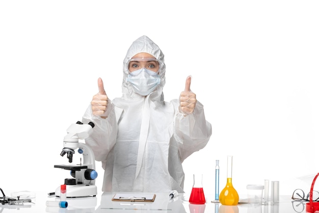 Front view young female doctor in white protective suit with mask due to covid showing like signs on white background virus pandemic splash covid-
