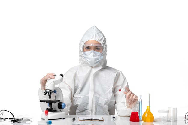 Front view young female doctor in white protective suit with mask due to covid on white desk pandemic covid- virus health