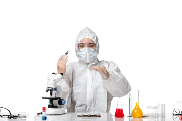 Front view young female doctor in white protective suit with mask due to covid working injection on a white background virus pandemic splash covid-