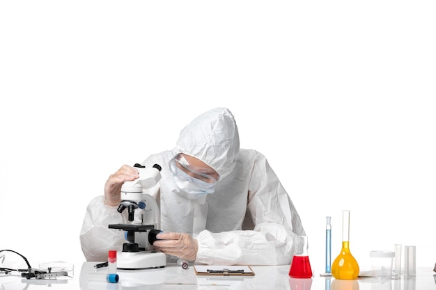 白い背景のウイルスパンデミックスプラッシュcovid-で顕微鏡で作業しているcovidのためにマスク付きの白い防護服を着た若い女性医師の正面図
