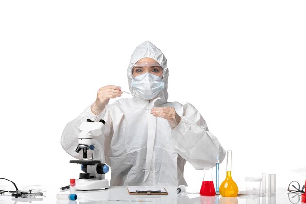 Front view young female doctor in white protective suit with mask due to covid working with solutions on light white background pandemic splash virus covid-