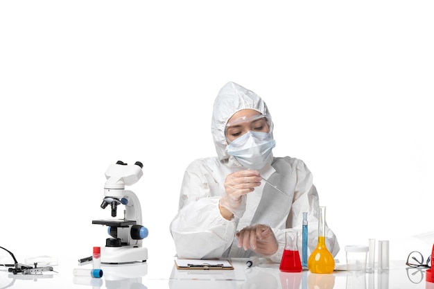 Вид спереди молодая женщина-врач в белом защитном костюме с маской из-за covid, работающей с растворами на белом фоне, пандемический всплеск вируса covid