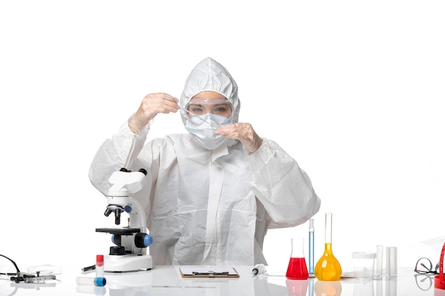 Front view young female doctor in white protective suit with mask due to covid working with solutions on white background pandemic splash virus covid