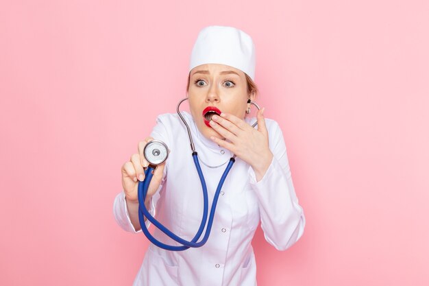 Front view young female doctor in white suit with blue stethoscope measuring on the pink space  female job