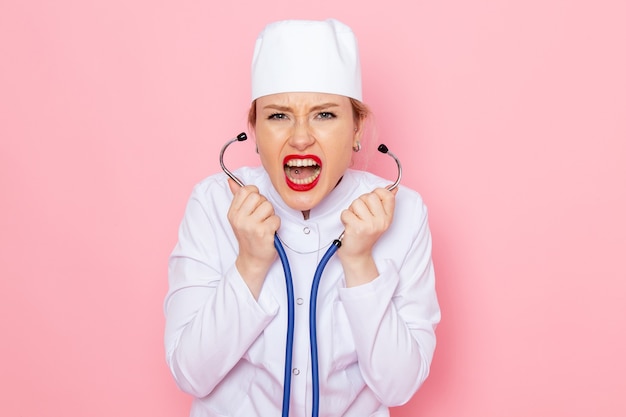 Medico femminile giovane vista frontale in vestito bianco con lo stetoscopio blu in posa urlando e misurando sul lavoro femminile medico ospedale medico medicina spazio rosa