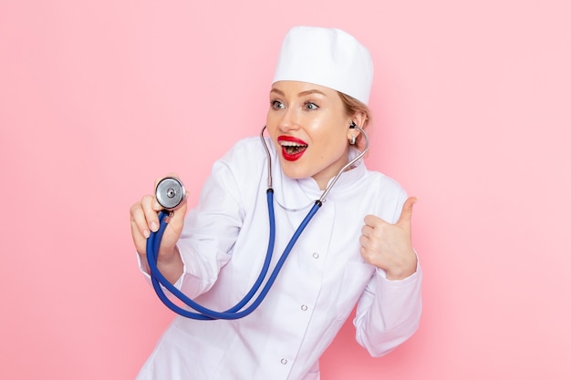 파란색 청진 포즈 웃 고 분홍색 공간 의학 의료 병원 의사 여성에 측정 흰색 정장에 전면보기 젊은 여성 의사