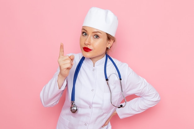 파란색 청진 기 포즈와 핑크 공간 여성 작업에 위협 흰색 정장에 전면보기 젊은 여성 의사