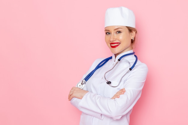 ピンクのスペースの仕事医学医療病院医師に笑顔でポーズ青い聴診器で白いスーツの正面の若い女性医師