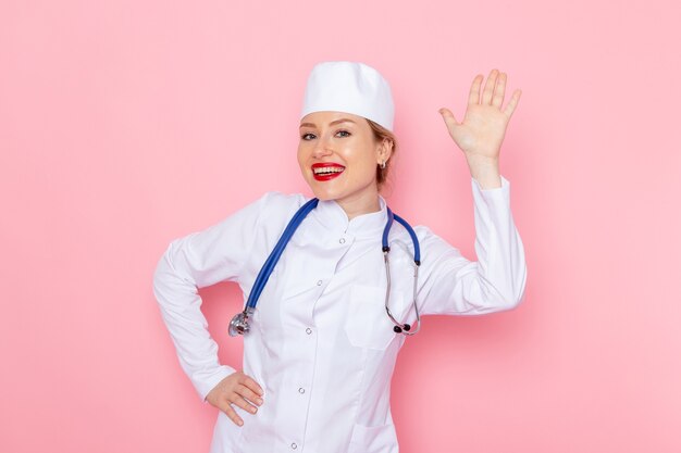 Front view young female doctor in white suit with blue stethoscope smiling and posing on the pink space medicine medical hospital doctor female