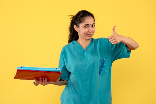 Front view of young female doctor with documents on yellow wall