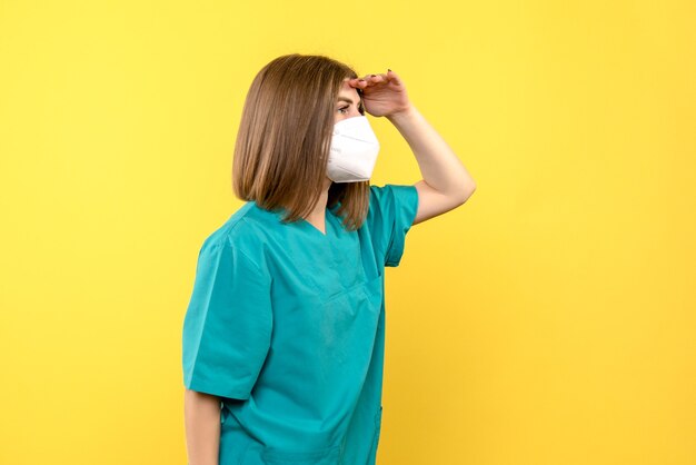 Front view of young female doctor with mask on yellow wall