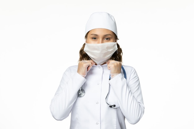 Вид спереди молодая женщина-врач с защитной маской из-за коронавируса и улыбается на белой поверхности