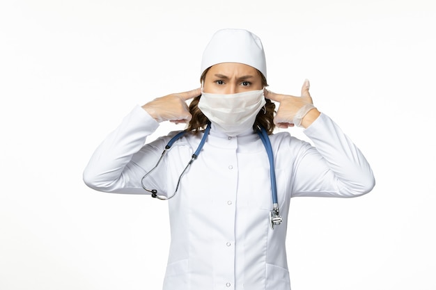 흰색 책상에 코로나 바이러스로 인해 보호 마스크가있는 전면보기 젊은 여성 의사