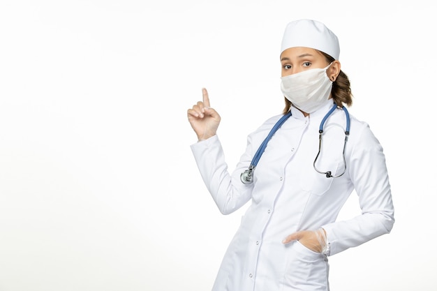 Вид спереди молодая женщина-врач со стерильной маской из-за коронавируса на светлой белой поверхности