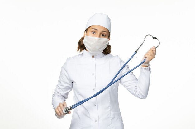 Front view young female doctor with sterile mask due to coronavirus on the light white surface