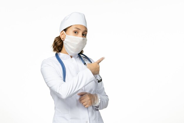 흰색 책상에 코로나 바이러스로 인해 멸균 마스크가있는 전면보기 젊은 여성 의사
