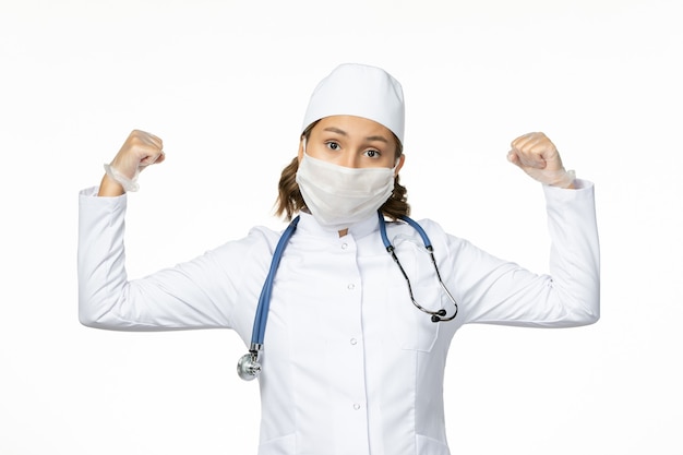 Front view young female doctor with sterile mask and gloves due to coronavirus flexing on white surface