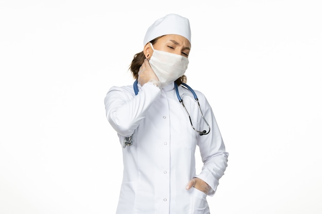 흰색 표면에 목 통증이있는 코로나 바이러스로 인해 멸균 마스크와 장갑이있는 전면보기 젊은 여성 의사