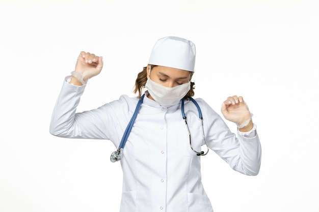 Free photo front view young female doctor with sterile mask and gloves due to coronavirus slightly dancing on white surface