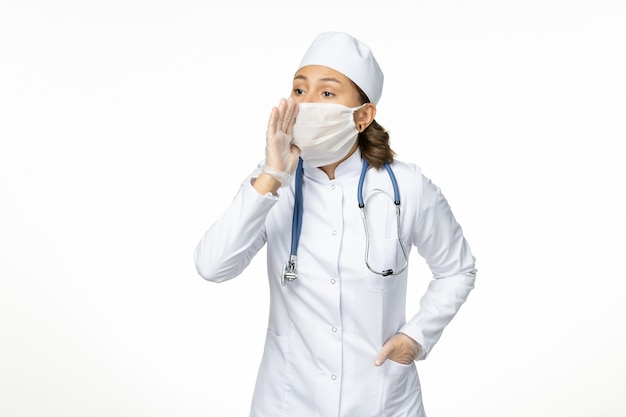흰색 표면에 속삭이는 코로나 바이러스로 인해 멸균 마스크와 장갑 전면보기 젊은 여성 의사