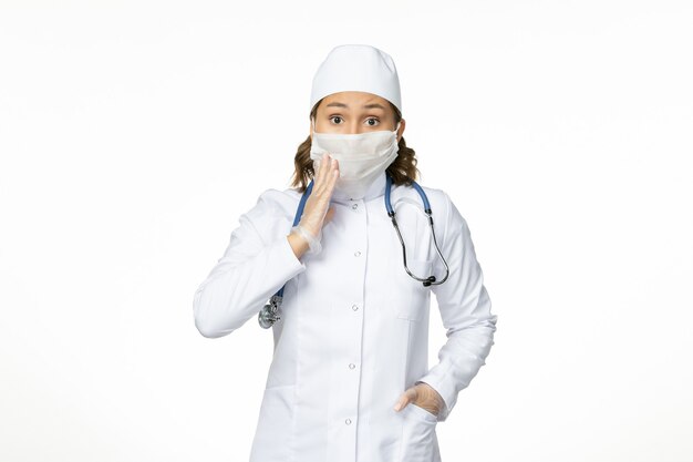 Front view young female doctor with sterile mask and gloves due to coronavirus on the white desk