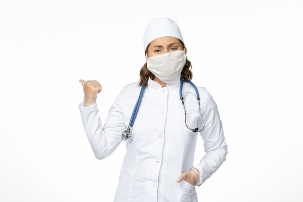 Front view young female doctor with sterile mask and gloves due to coronavirus on white desk