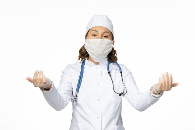 Front view young female doctor with sterile mask and gloves due to coronavirus on white desk